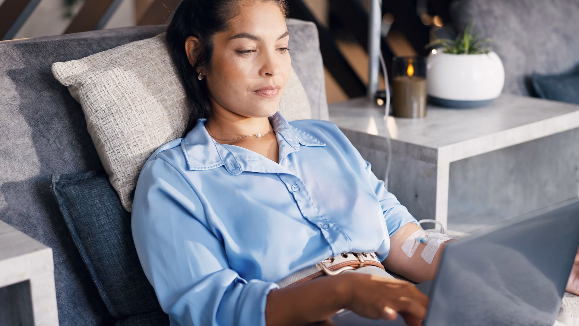 Patient relaxing in a comfortable chair while receiving an iron infusion through an IV cannula, using a laptop during treatment.