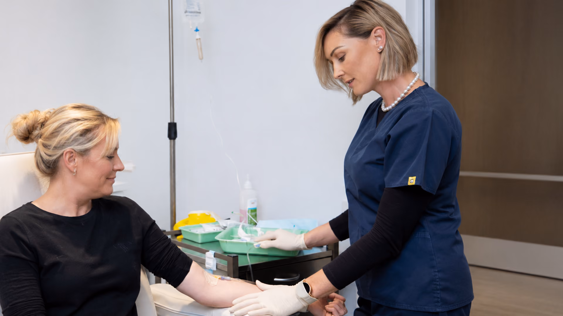 Nurse assisting a patient receiving an iron infusion through an IV cannula while seated comfortably in a treatment chair.