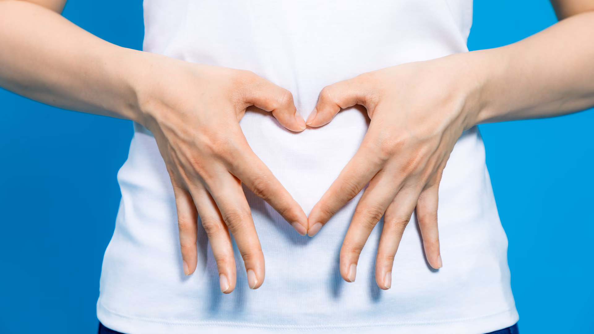 Person forming a heart shape over their abdomen with both hands to represent digestive health and gut wellbeing.