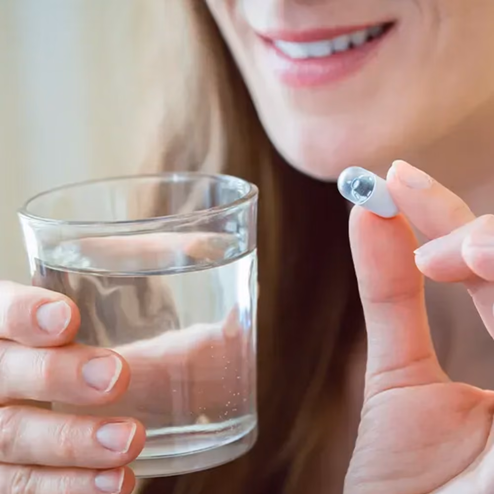 Person holding a PillCam capsule and a glass of water before swallowing it for a capsule endoscopy procedure.