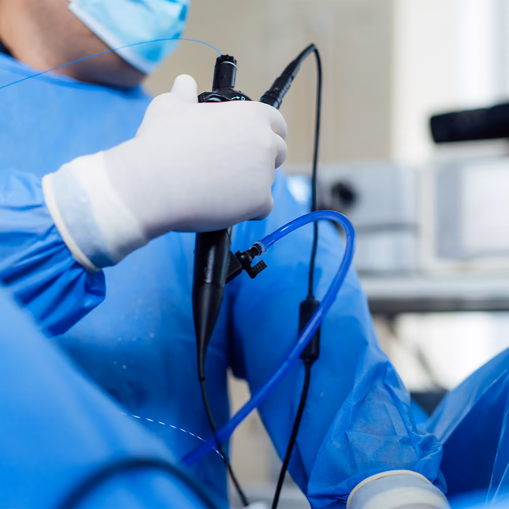 Clinician holding an endoscope during an endoscopy procedure in a hospital treatment room.