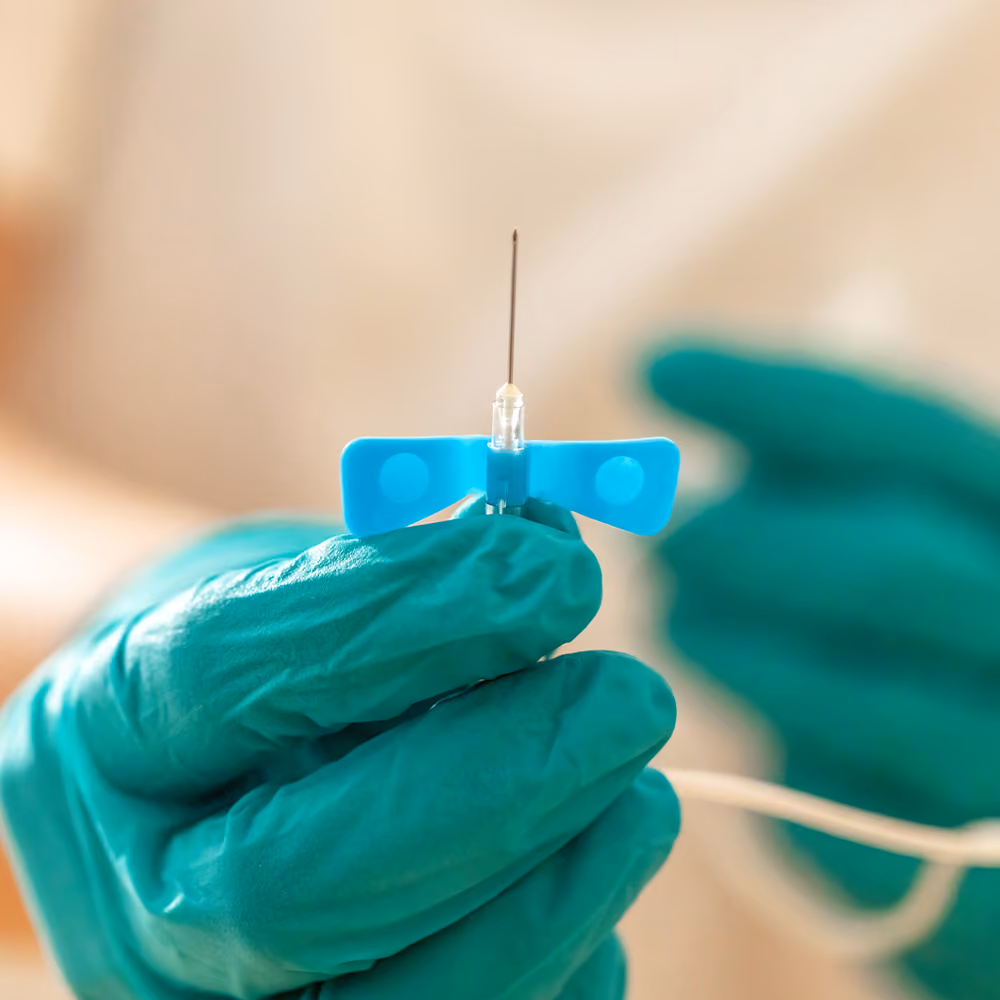 Close-up of a clinician holding a sterile intravenous cannula ready for a vitamin infusion procedure.