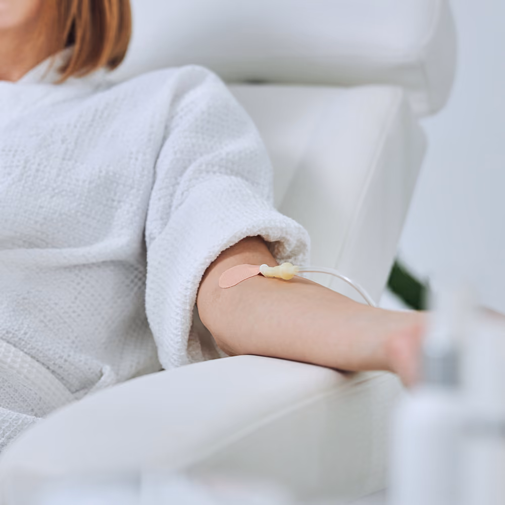 Patient receiving a vitamin C infusion through an IV cannula while relaxing in a treatment chair.