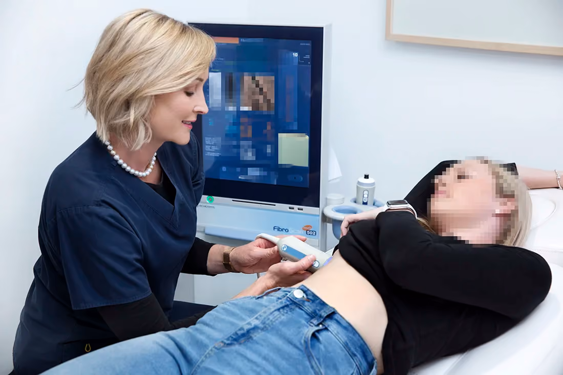 A nurse wearing blue scrubs doing a liver scan on a female patient.