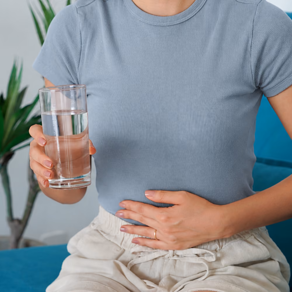 Person holding a glass of water with a hand on their abdomen, illustrating that the PillCam capsule passes naturally through the digestive system.