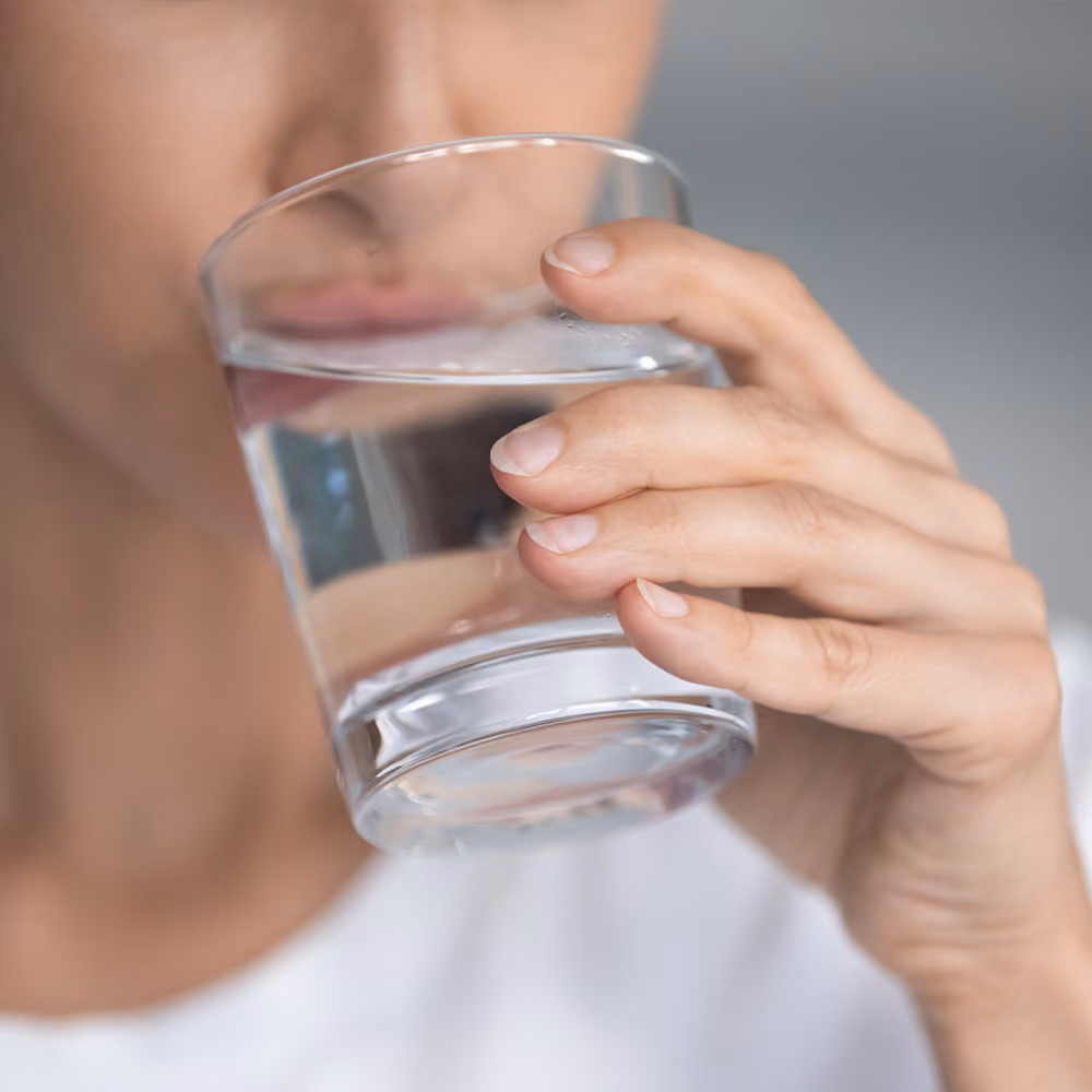 Person drinking a glass of water to stay hydrated before or after a vitamin infusion.