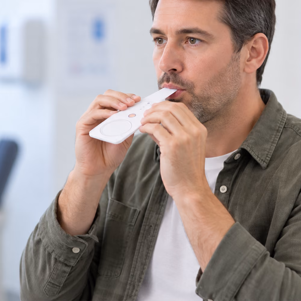 A patient blows into a silver foil bag for a urea breath test, assisted by a gloved medical professional in a clinic.