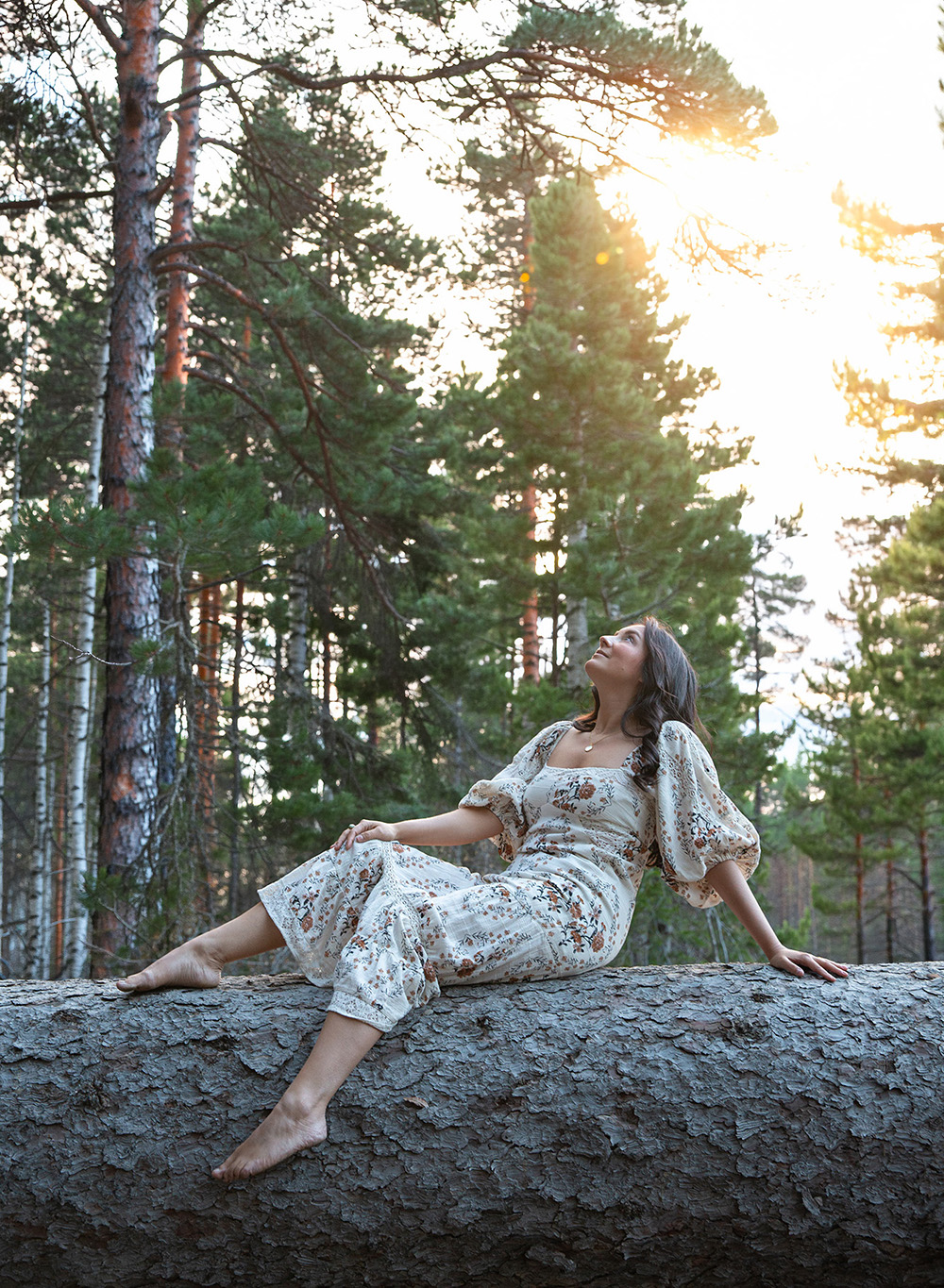Elaine sitting on a log in a forest at sunset looking up at the sunlight