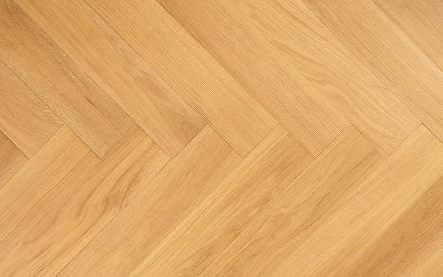 Close-up of wooden parquet flooring arranged in a herringbone pattern with a light oak finish.