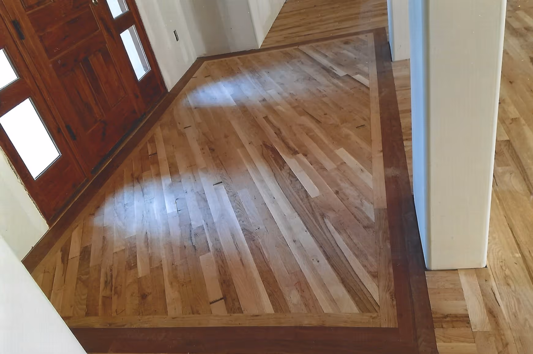 Wooden floor with a dark wood border in front of a red-brown door with glass panels.
