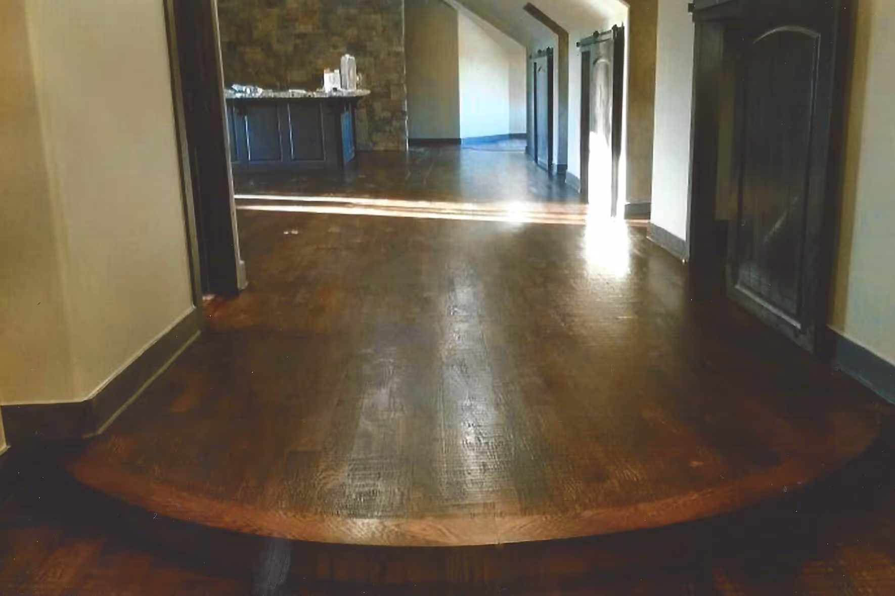 Empty room with polished dark wood flooring and a stone accent wall at the back with a counter.