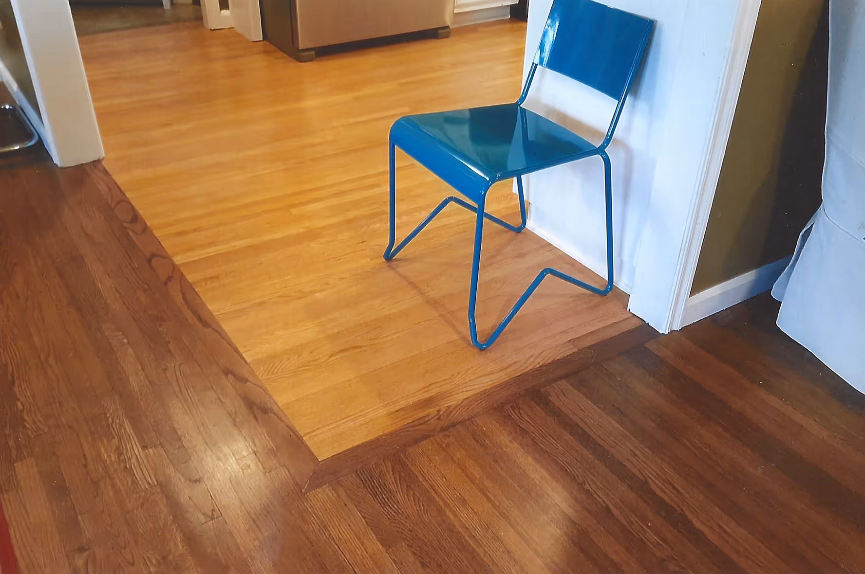 Blue metal chair placed on a transition area between two differently stained hardwood floors in a room.
