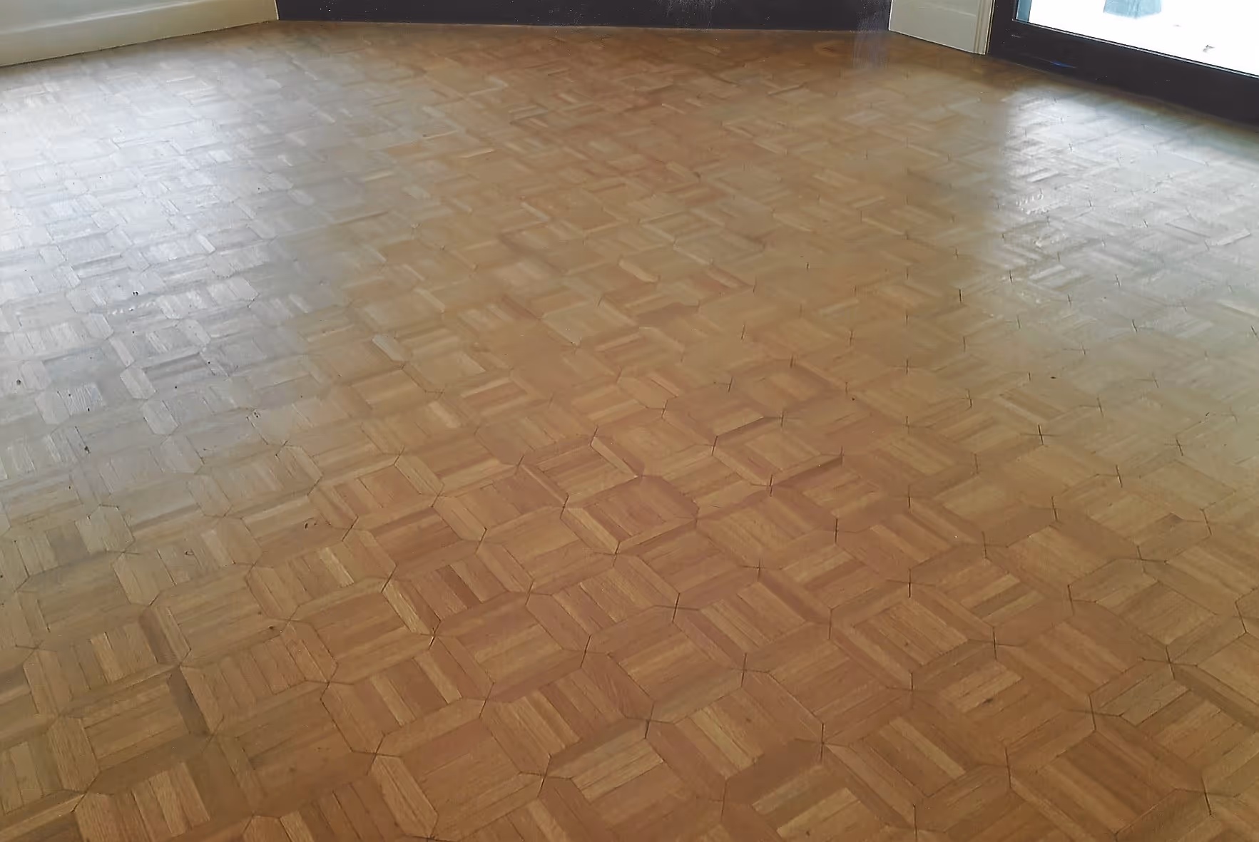 Wooden parquet floor with a geometric hexagonal pattern in an empty room with light coming through windows.