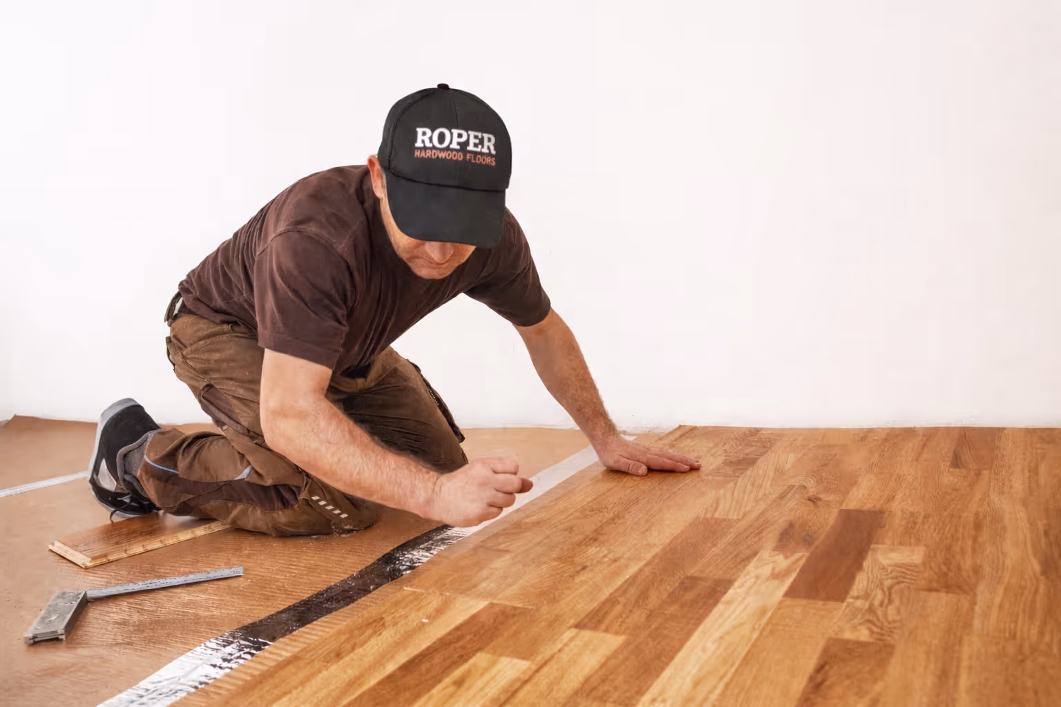 Worker installing hardwood flooring while kneeling on the floor and aligning wood planks.