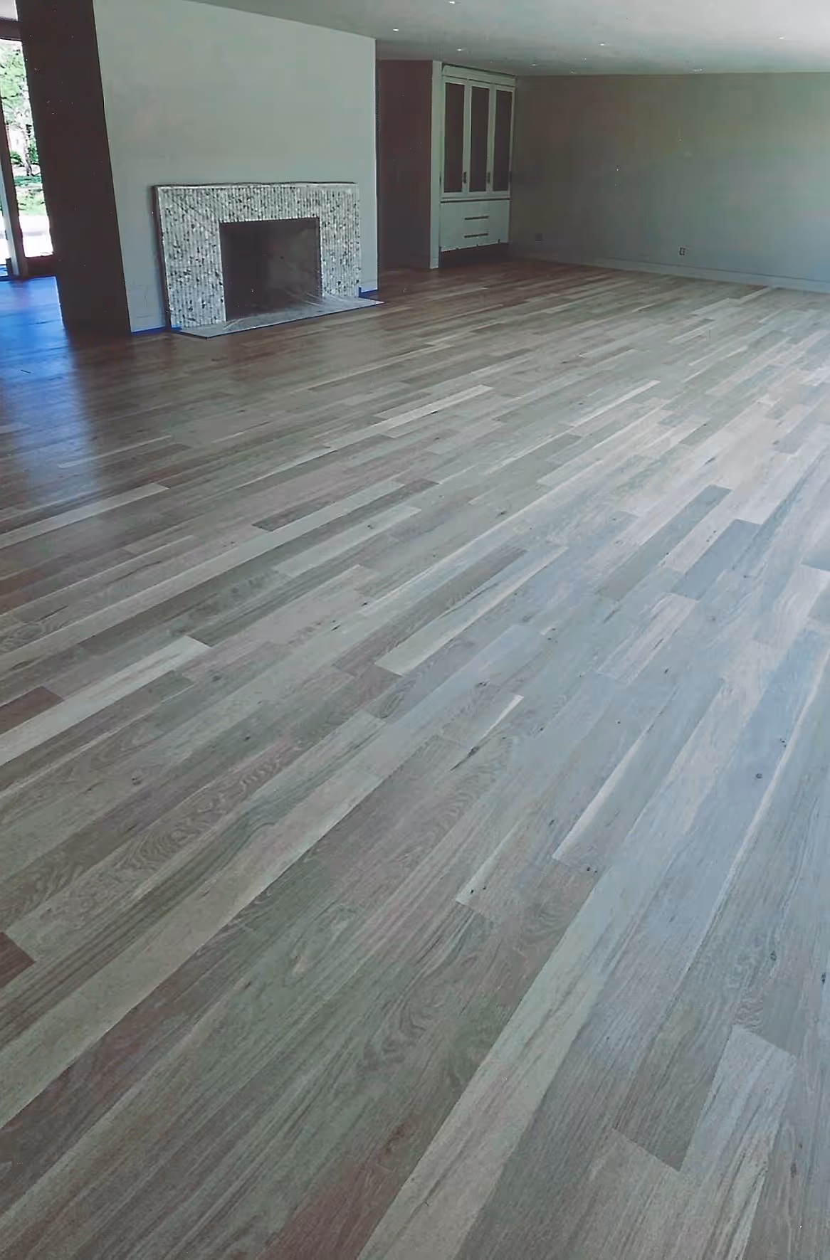 Empty room with light wood flooring, a fireplace with mosaic tile surround, and built-in cabinets against neutral walls.
