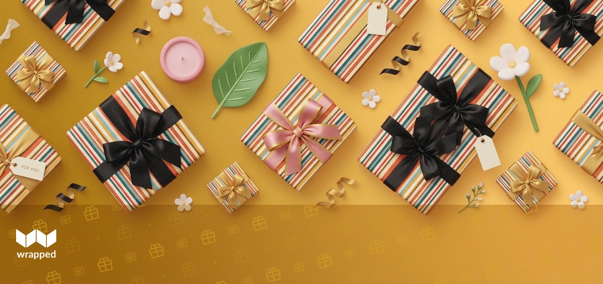 A lit candle in a gift box surrounded by wrapping paper and a handwritten card on a wooden table