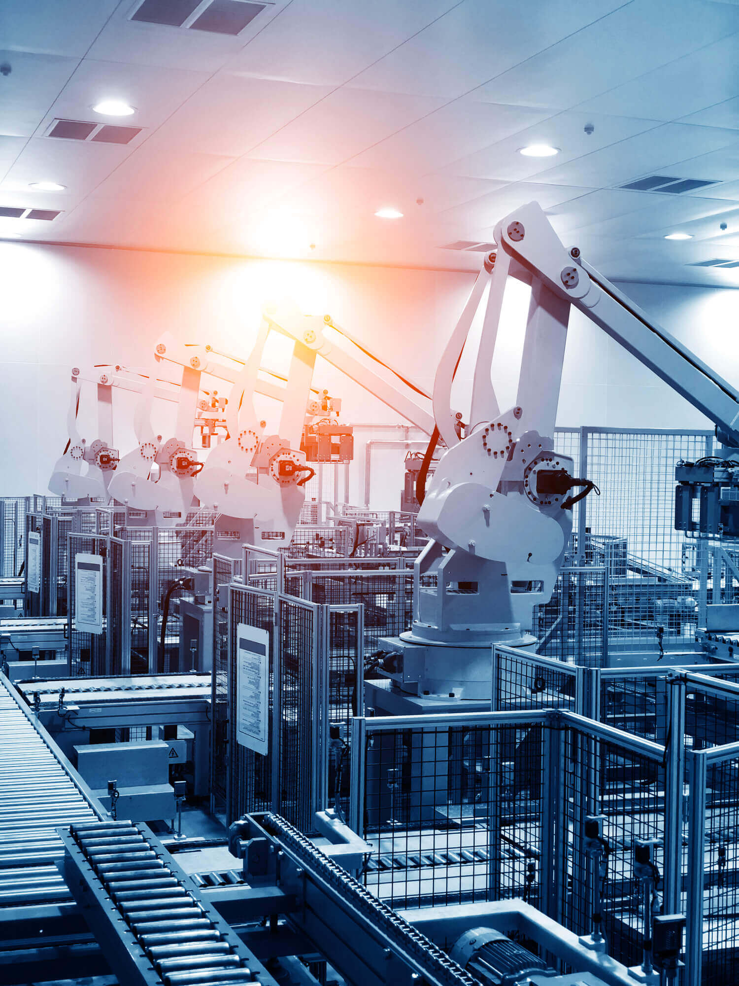 Row of white industrial robotic arms aligned in a modern factory setting with conveyor belts and metal safety fencing under bright ceiling lights.