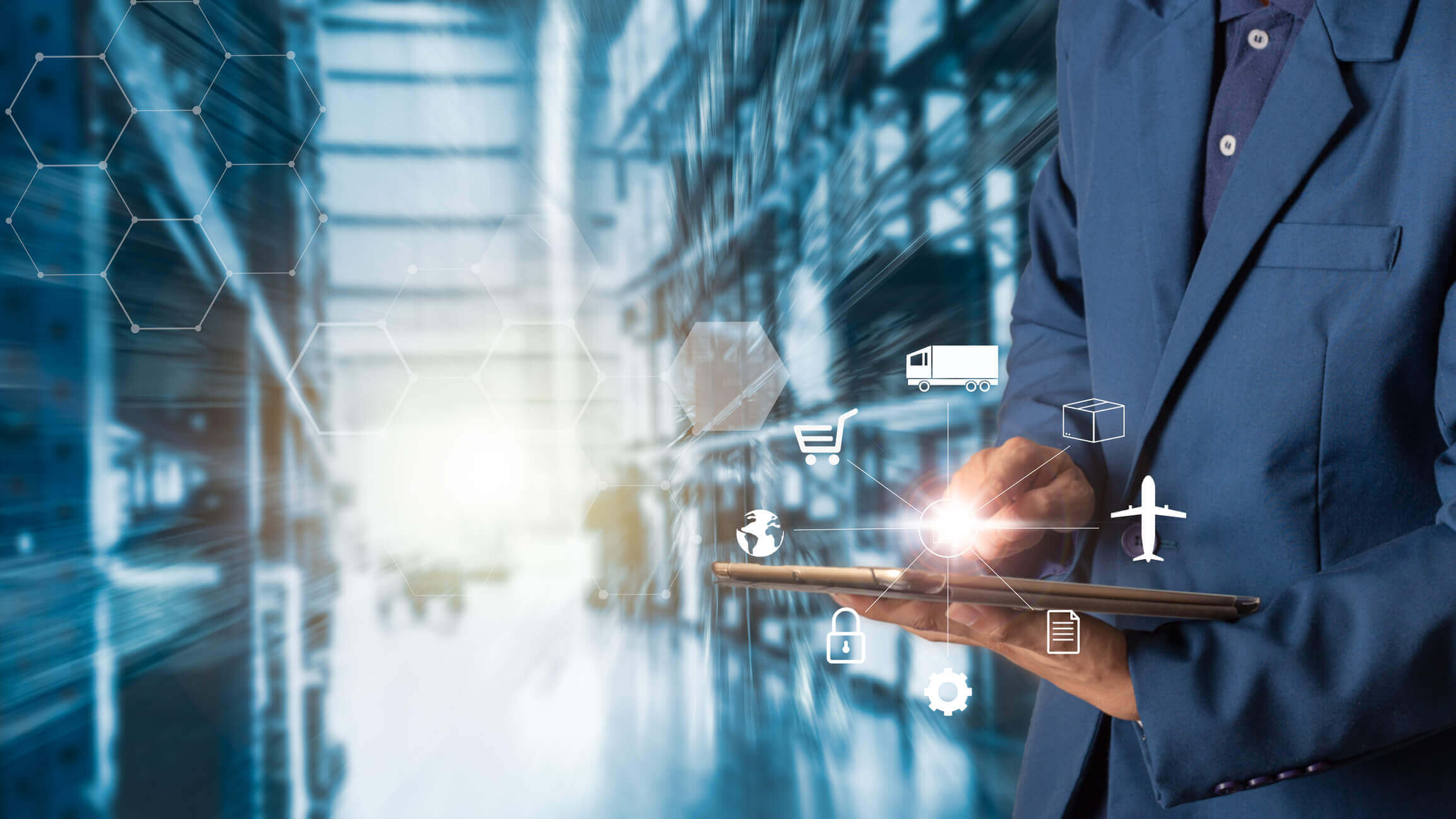 Person in blue suit using a tablet with overlaid icons related to logistics and supply chain, including a truck, shopping cart, airplane, package, document, lock, gear, and globe, set against a blurred industrial warehouse background.