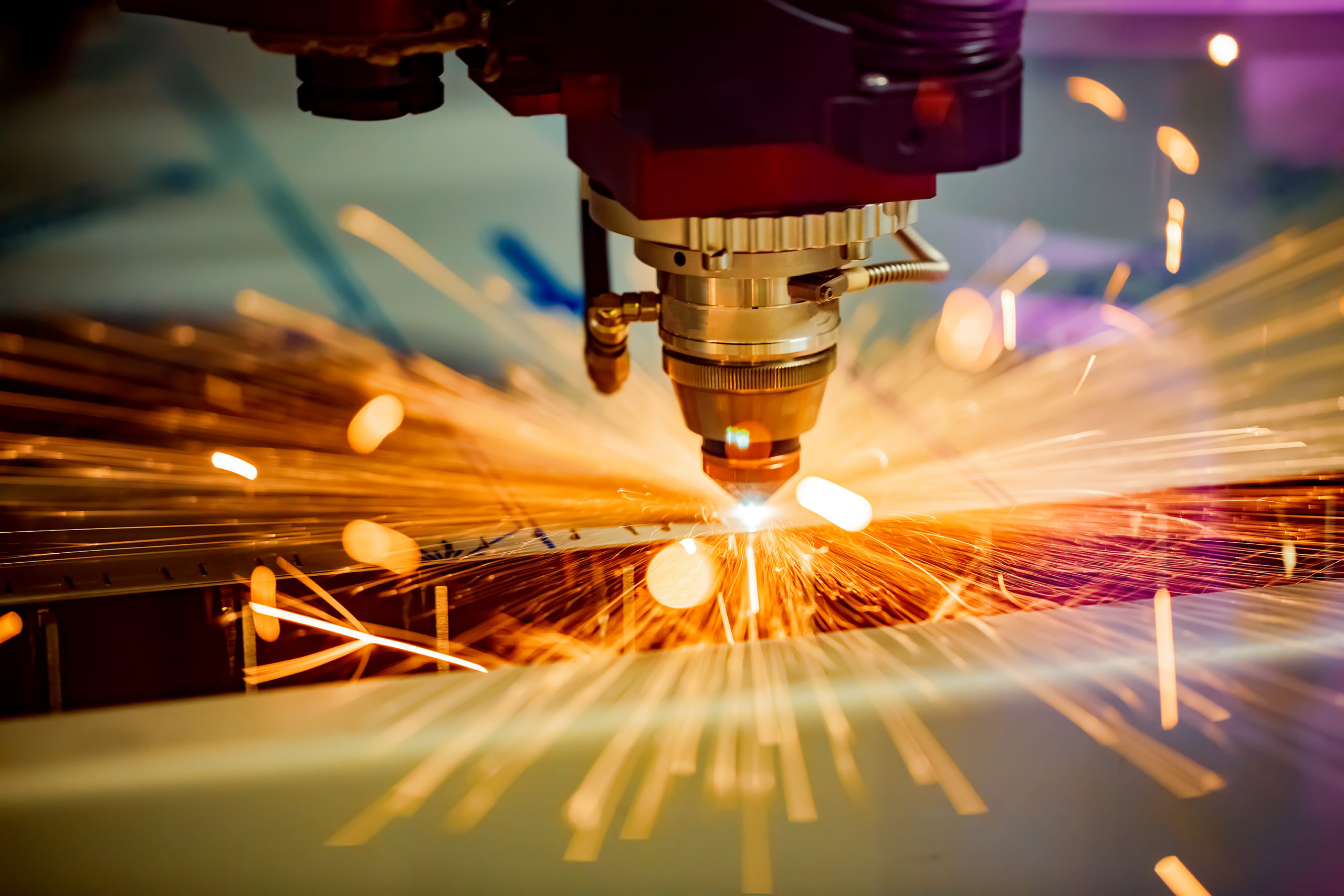 Close-up of a laser cutting machine producing bright orange sparks while cutting metal.