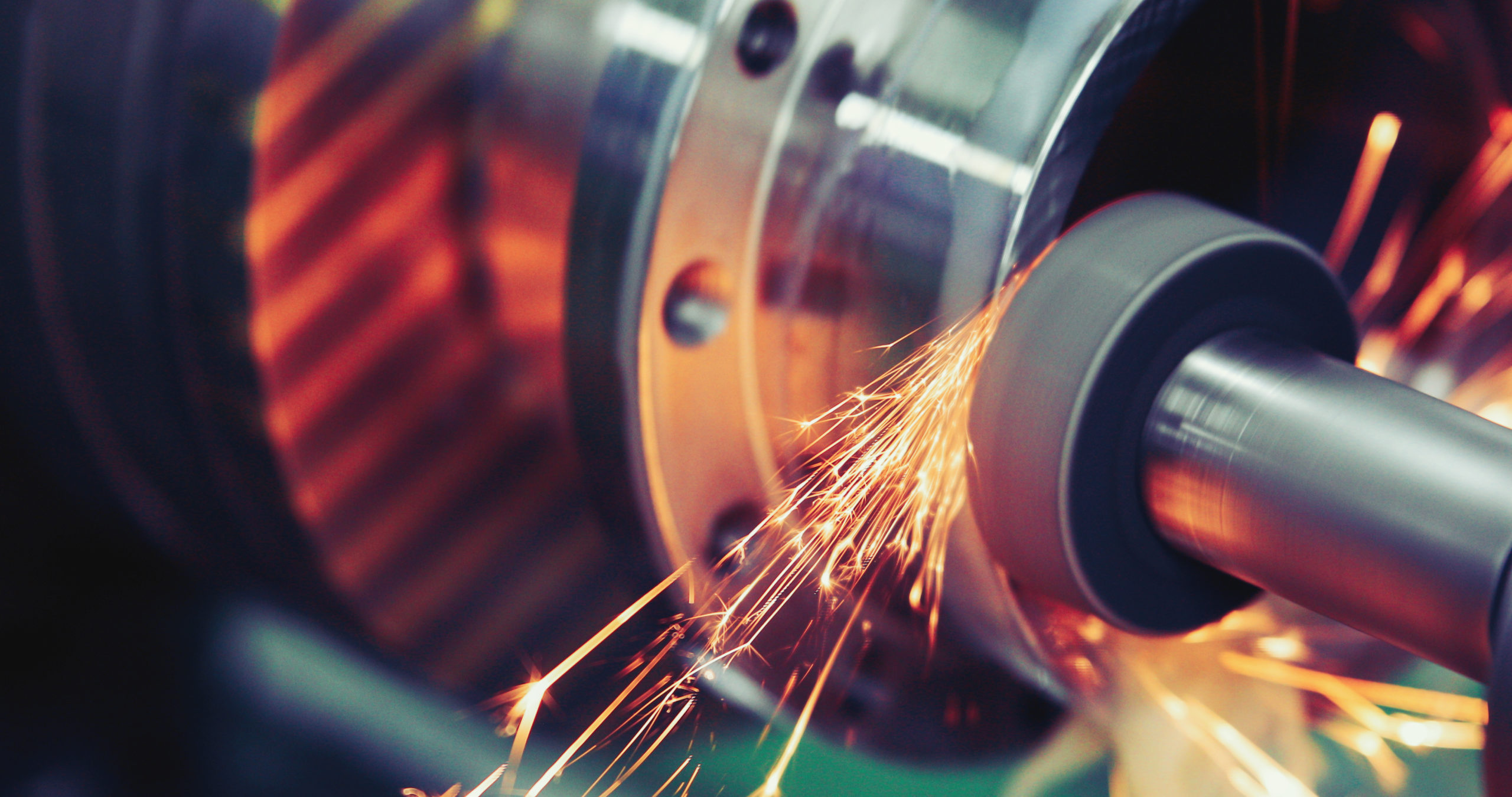 Close-up of a metal grinding process producing sparks as the grinding wheel sharpens the cylindrical metal surface.