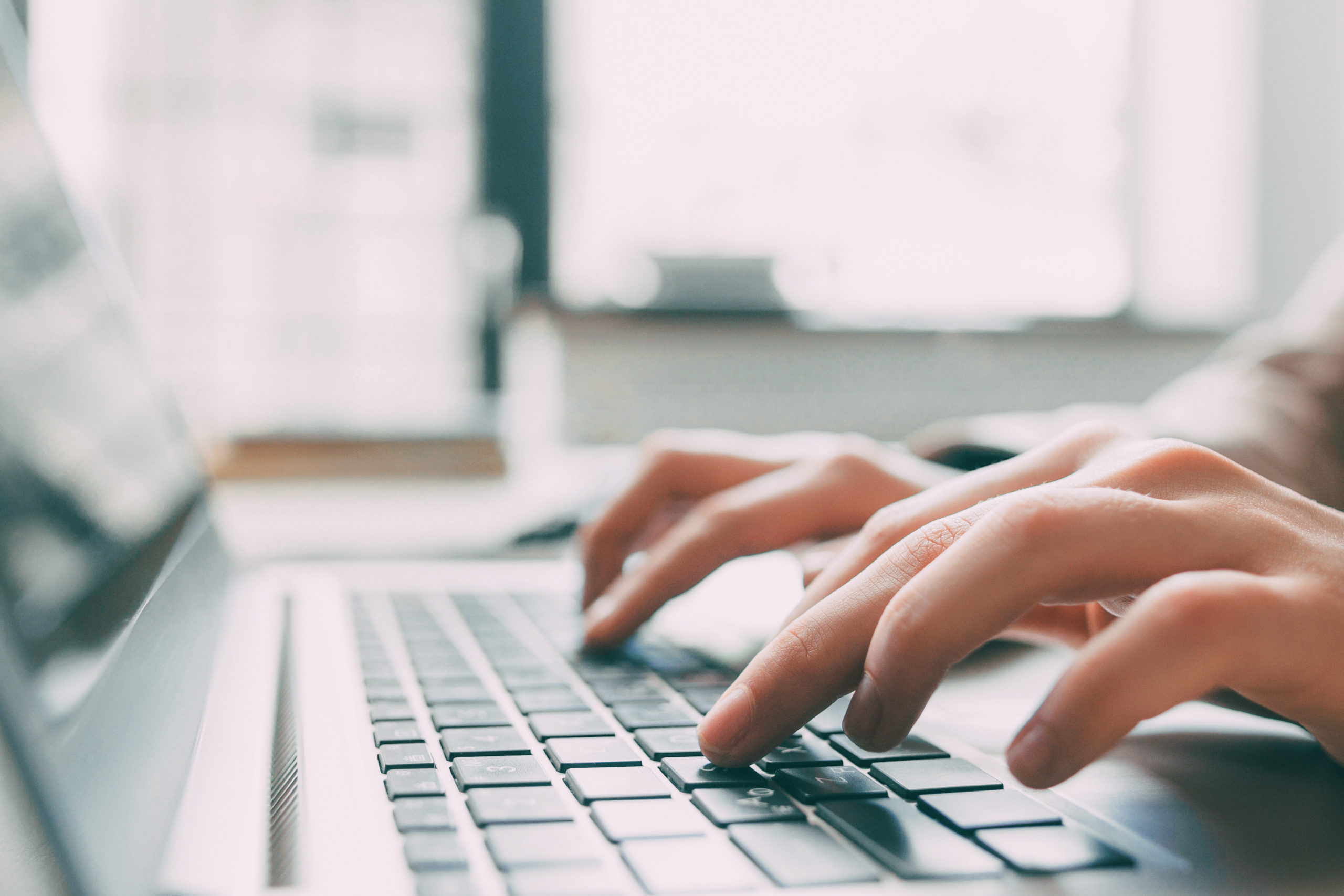 Close-up of hands typing on a laptop keyboard in a softly lit indoor setting with a blurred background.