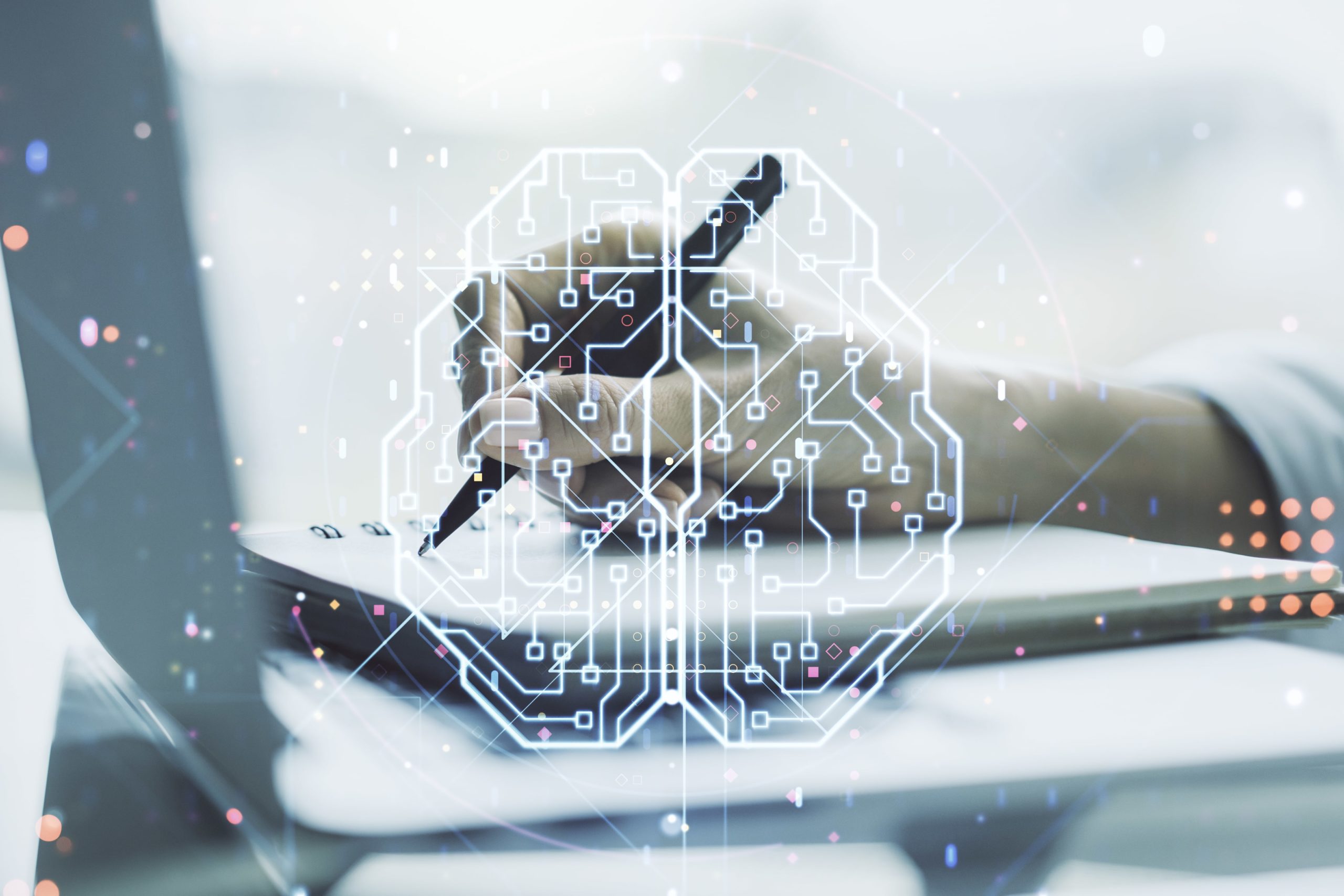 A hand holding a pen writing on paper beside a laptop keyboard, overlaid with a glowing digital circuit pattern shaped like a brain, symbolizing artificial intelligence and technology.
