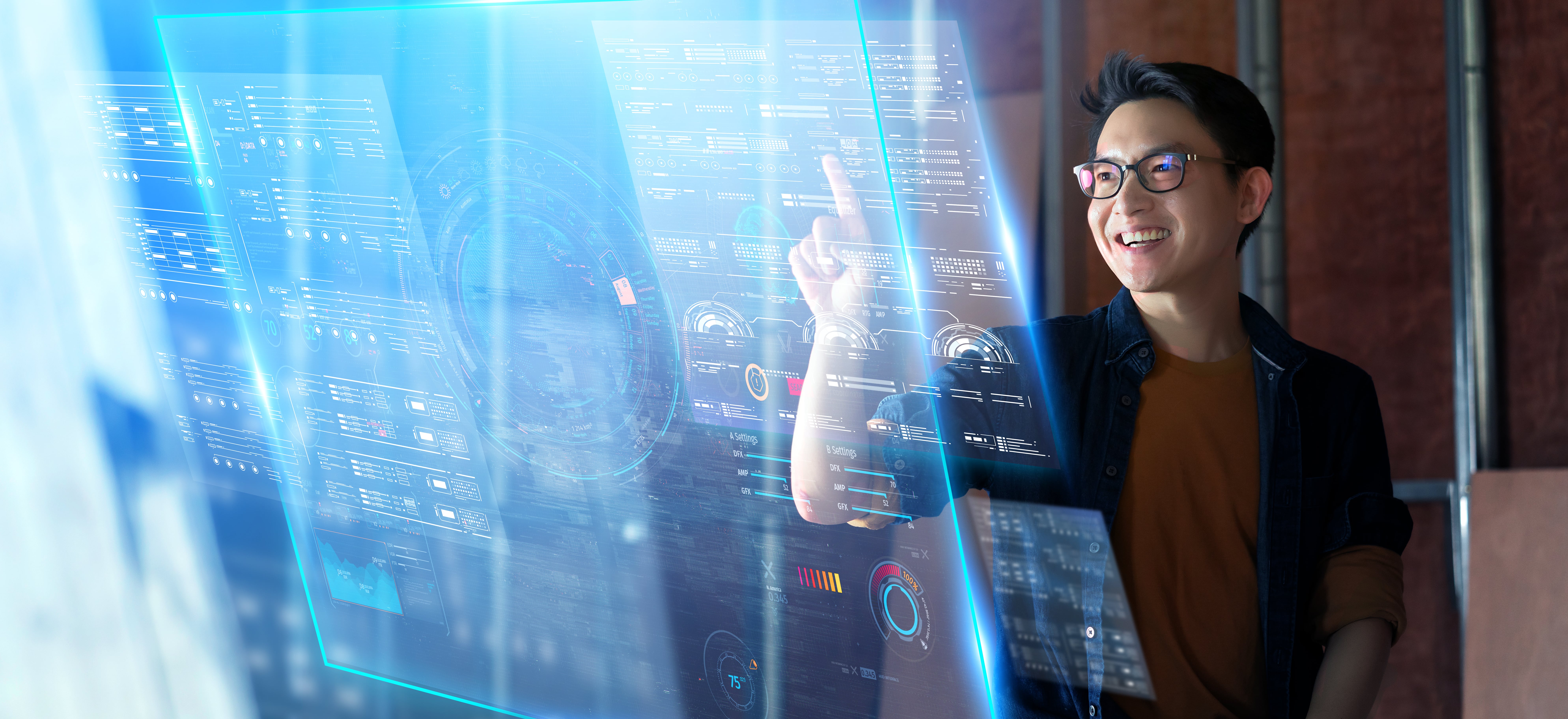 A smiling man wearing glasses interacts with a large transparent digital interface displaying futuristic data and charts in a high-tech environment.