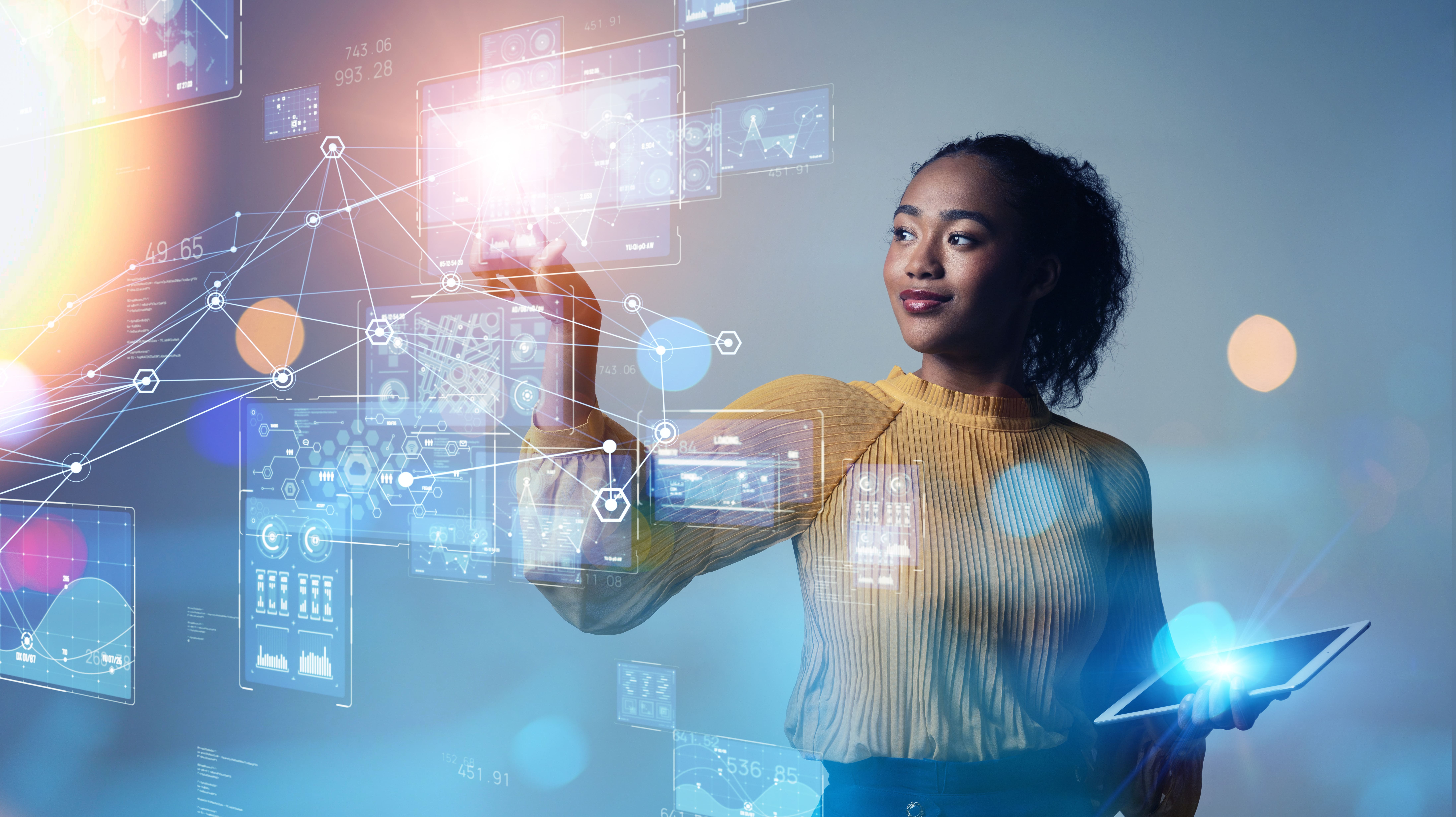 Young woman holding a tablet in one hand and interacting with floating digital data charts and network connections with the other hand against a gray background.
