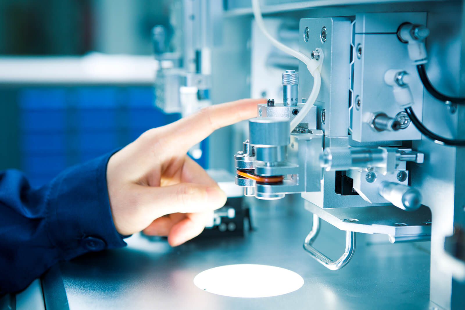Hand operating or adjusting a precision part of a high-tech machine or laboratory equipment with various metal components and tubes.