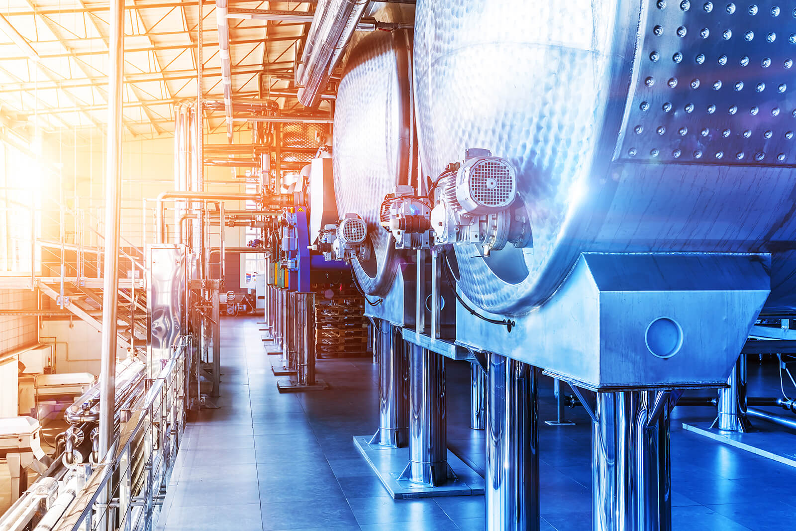 Row of large industrial stainless steel tanks with motors in a bright, modern factory setting.