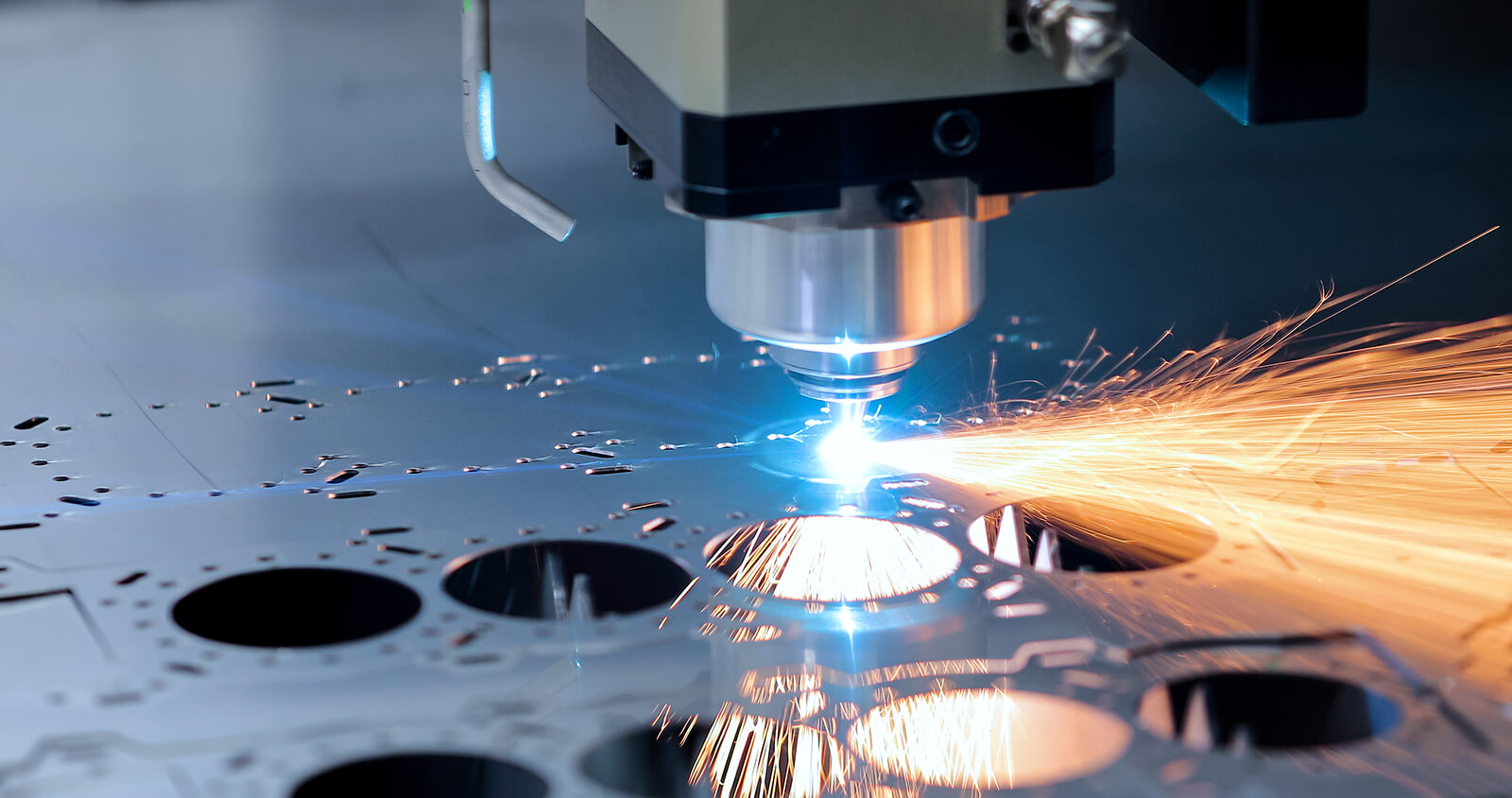 Close-up of a CNC laser cutting machine producing sparks as it cuts circular holes in a metal sheet.