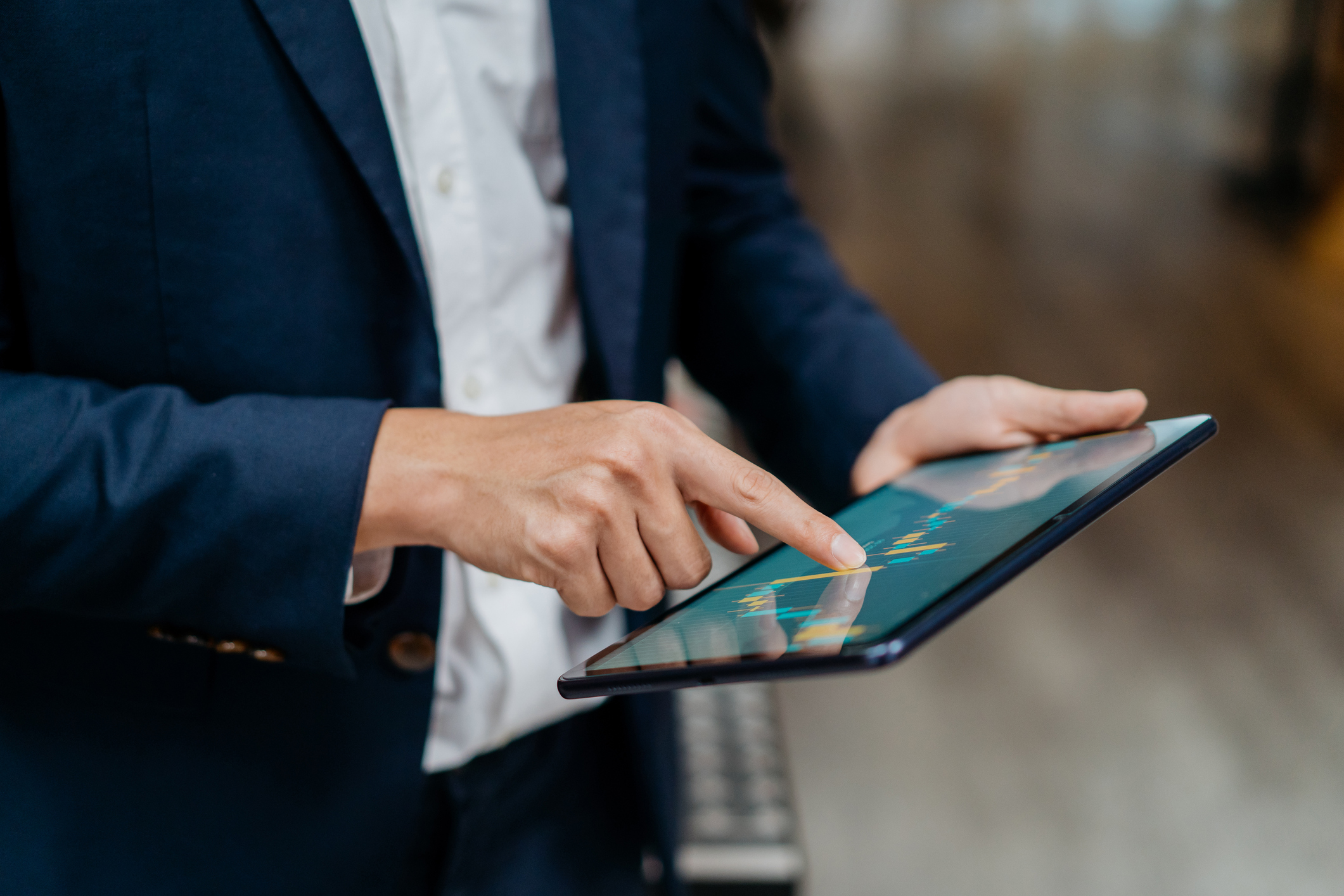 Person wearing a navy blue suit using a tablet displaying financial charts with colorful candlesticks and trend lines.