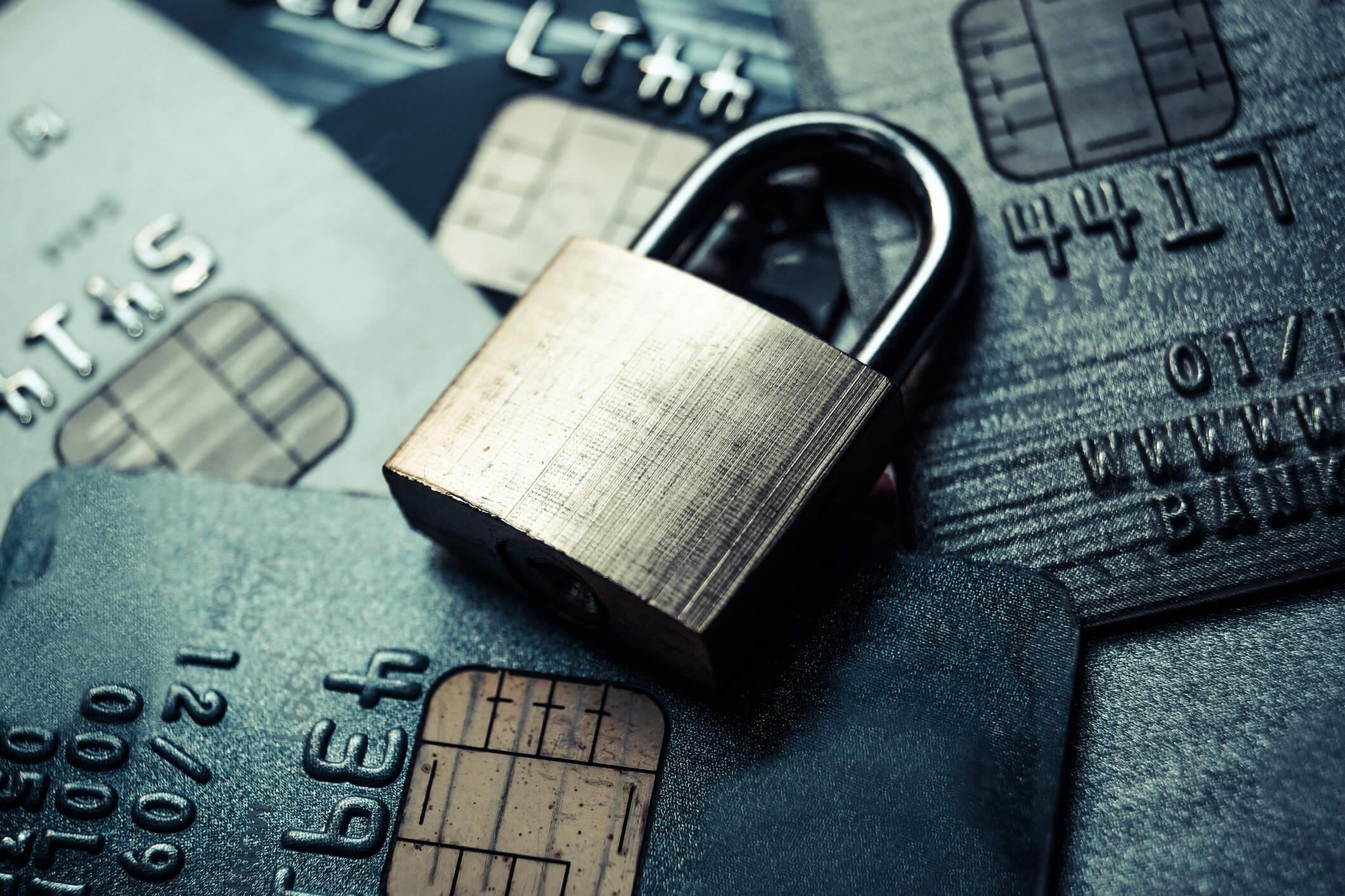 A brass padlock placed on top of several overlapping credit cards with visible chip icons and embossed numbers, symbolizing security and protection of financial information.