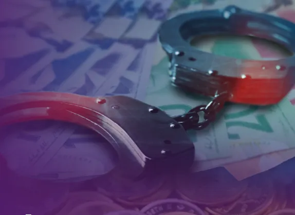 Metal handcuffs resting on scattered banknotes and coins, symbolizing crime and financial crime themes.