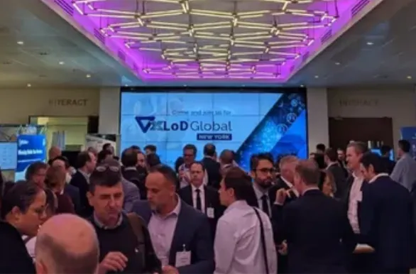 Crowd of business professionals networking in a conference room with a large digital screen displaying 'Join XLoD Global New York' and a purple ceiling light fixture above.