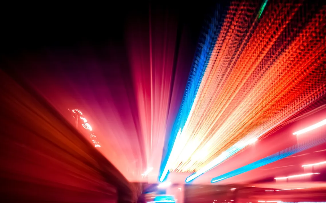 Blurred light trails in red, blue, and white colors streaking diagonally across a dark background, creating a dynamic abstract effect.