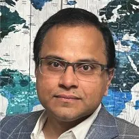 Man wearing glasses and a checkered blazer, posing in front of a world map wall.
