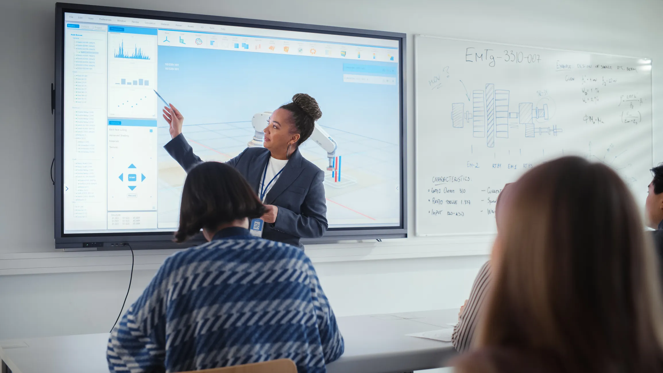 Female presenter points at a large screen with graphs and a robotic arm simulation while an audience watches in a classroom with engineering diagrams on a whiteboard.