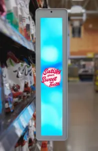 Vertical digital display in a grocery store aisle with colorful packaging on shelves and the message 'Satisfy Your Sweet Tooth' in the center on a bright blue background.