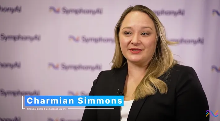 A woman with long blonde hair wearing a black blazer and white top is speaking. A text overlay identifies her as Charmian Simmons, Financial Crime & Compliance Expert. The background features a repeating SymphonyAI logo.