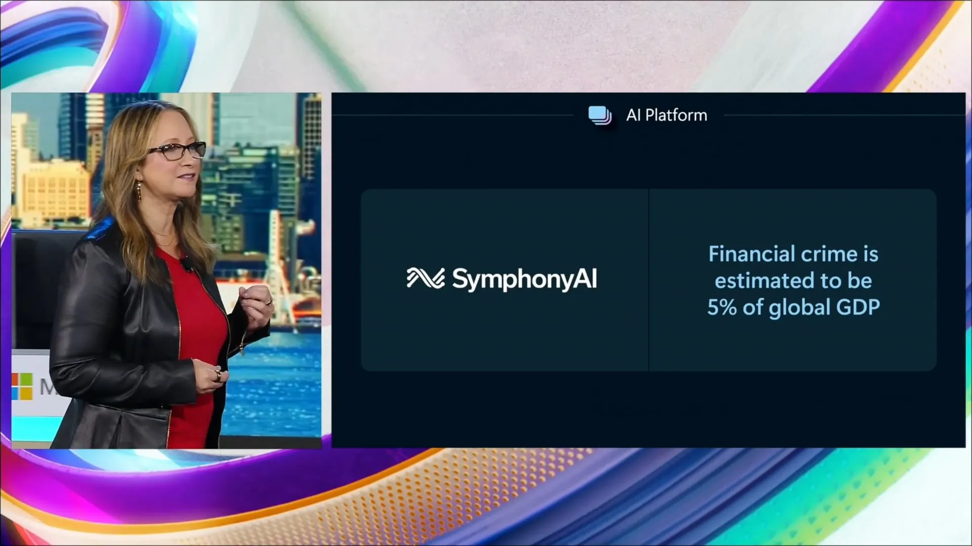 A woman wearing glasses, a red top, and a black leather jacket stands speaking in front of a colorful backdrop; beside her is a screen showing the SymphonyAI logo and the text 'Financial crime is estimated to be 5% of global GDP' under the heading 'AI Platform'.