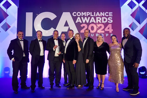 Group of nine people dressed in formal evening attire standing on stage at the ICA Compliance Awards 2024 Europe event, smiling and posing for a photo.