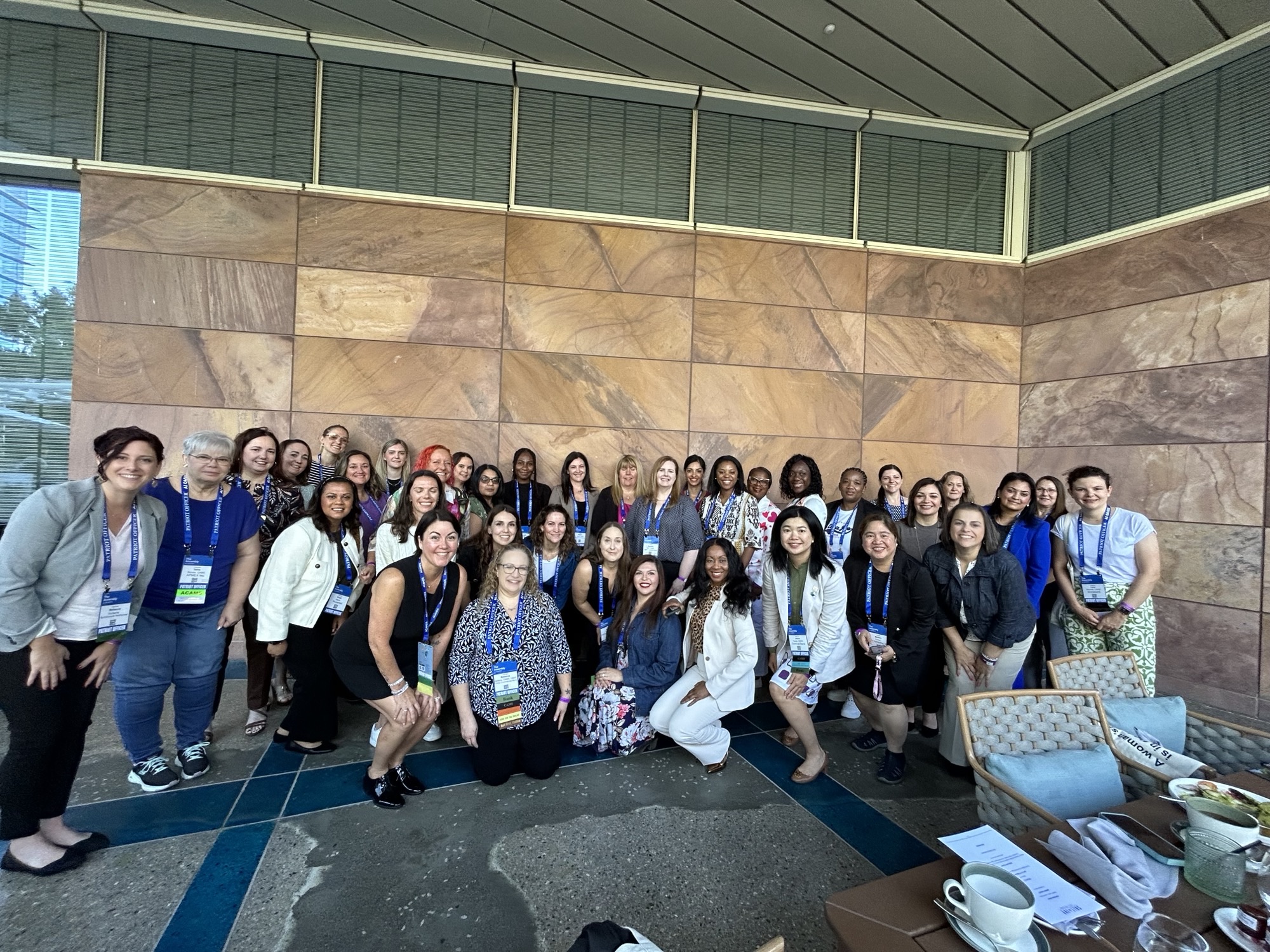 A group of women in fincrime smiling and posing for a photo in front of a wall during the Women’s Breakfast event hosted by SymphonyAI at the ACAMS Assembly 2024.