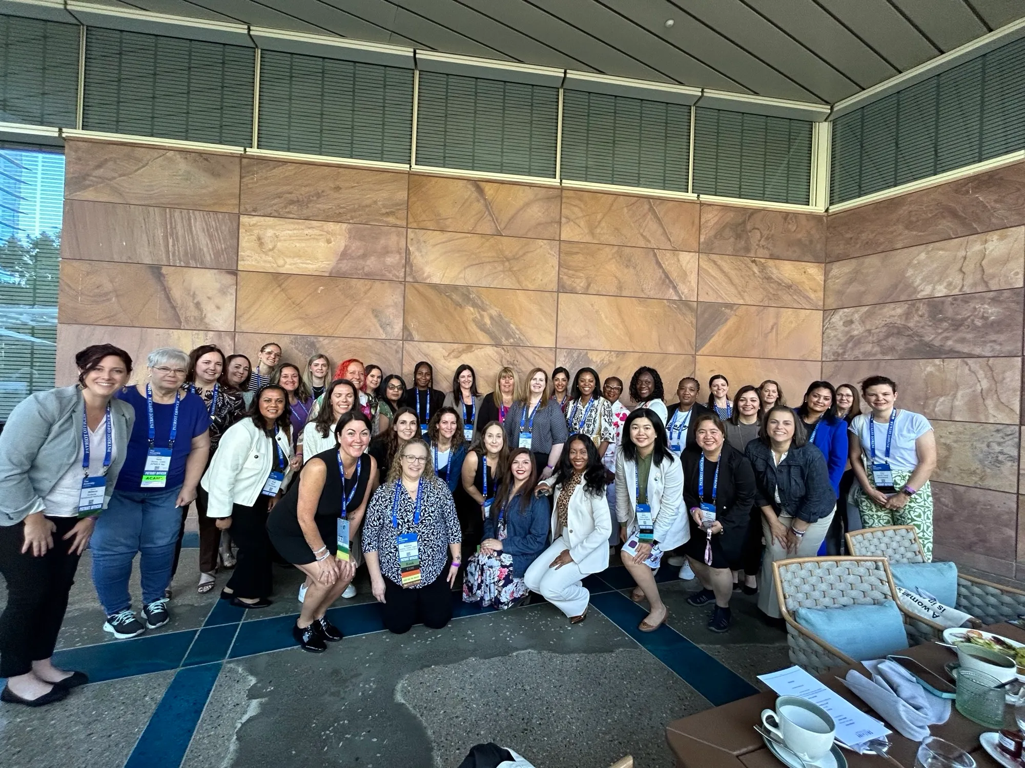 A group of women in fincrime smiling and posing for a photo in front of a wall during the Women’s Breakfast event hosted by SymphonyAI at the ACAMS Assembly 2024.