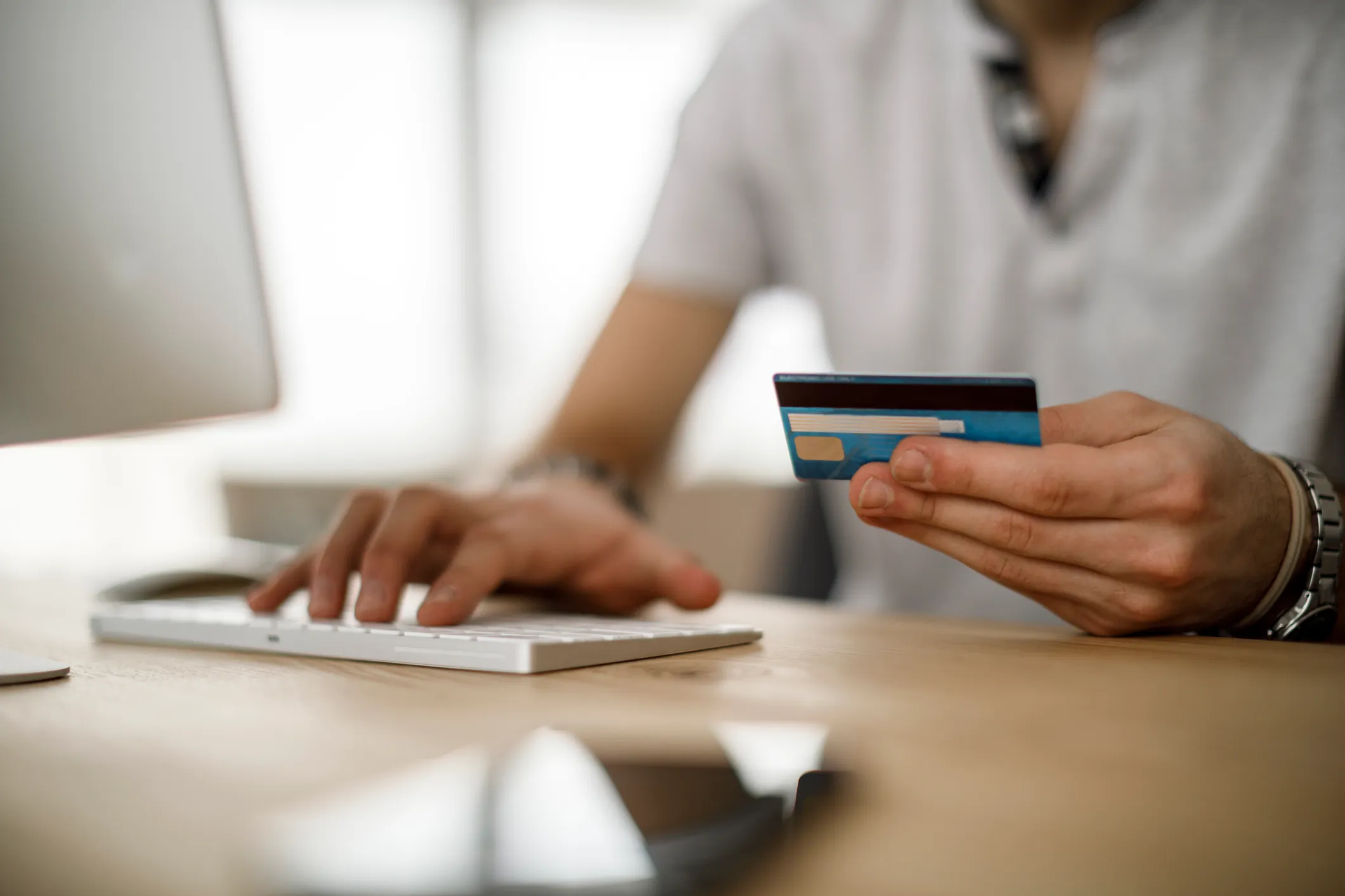 Person holding a credit card in one hand and typing on a keyboard with the other at a desk.