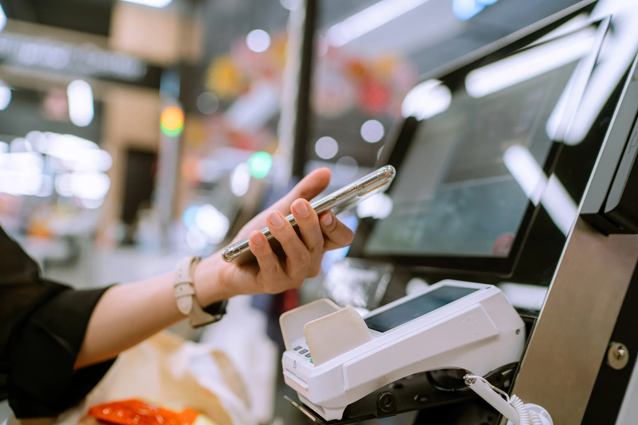 Person holding a smartphone near a card payment terminal at a checkout counter, using contactless payment.