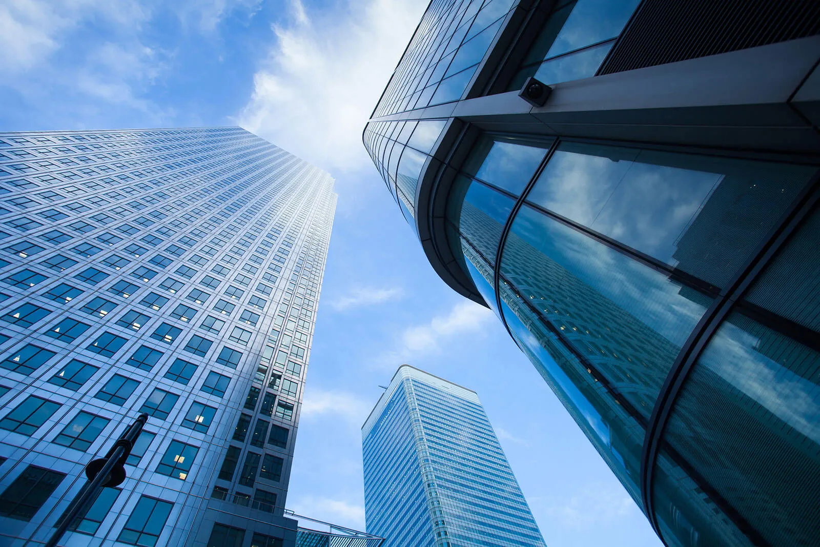 Low-angle view of three modern skyscrapers with reflective glass windows under a partly cloudy blue sky.