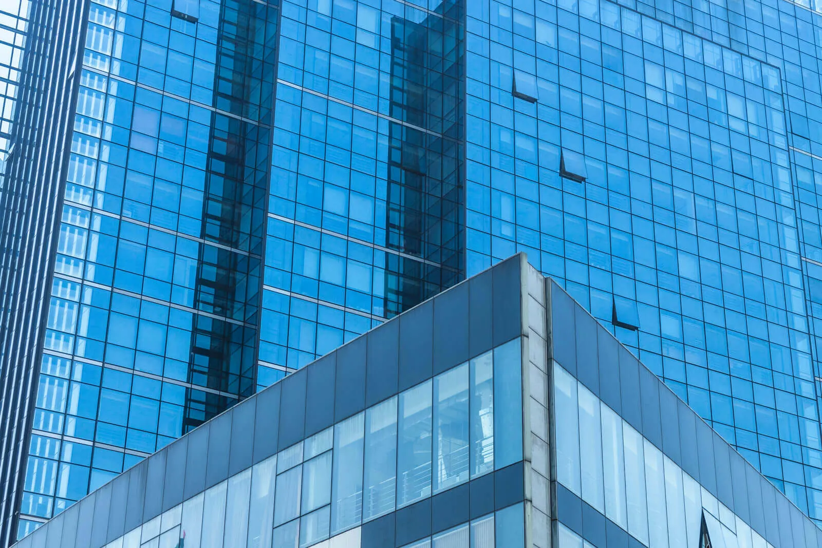Modern blue glass skyscraper with a focus on the corner section showing reflections and partially open windows.