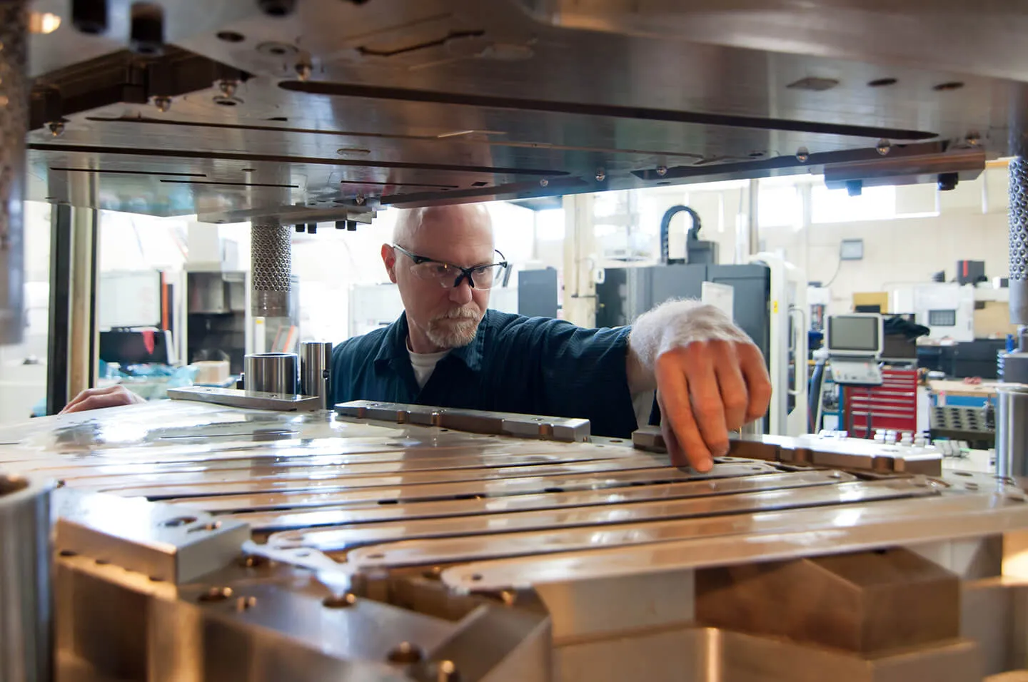 Man wearing safety glasses working on a large industrial metal machine part inside a manufacturing facility.