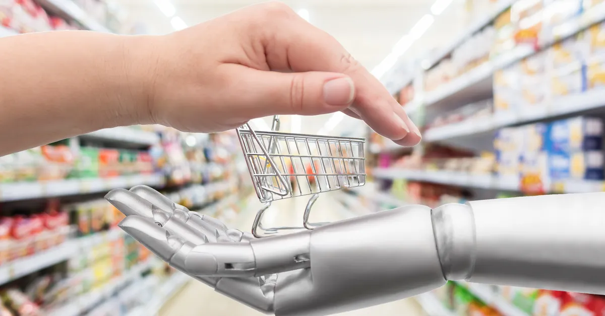 A human hand holding a small shopping cart being placed into the open palm of a robotic hand in a grocery store aisle.